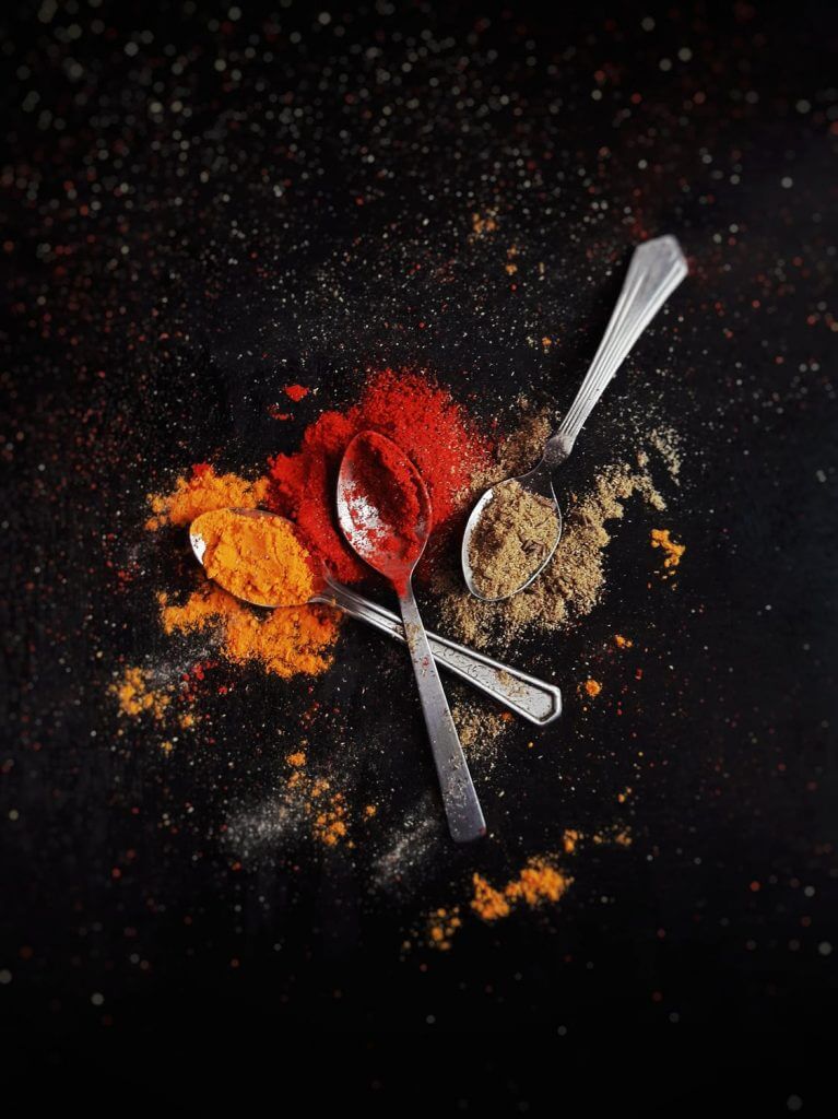 Orange, red, and green powder and spoons on black backgound